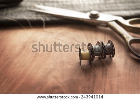 Old sewing machine bobbins with gold ( brass ) scissors and black silky fabric on a old grungy work table. Tailor's work table. textile or fine cloth making.