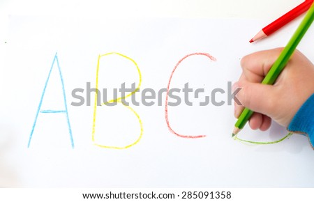 Close up of the hands of a little child writing letters with color pencils