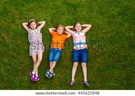 Happy children having fun outdoors. Kids playing in summer park. Little boy and two girls laying on green fresh grass