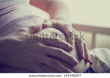Closeup of pregnant woman holding her hands on her swollen belly shaping a heart, toned retro or instagram effect.