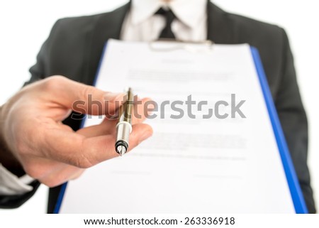 Businessman or salesman handing over a contract attached to a clipboard for signature offering a ballpoint pen in his hand with focus to the pen.