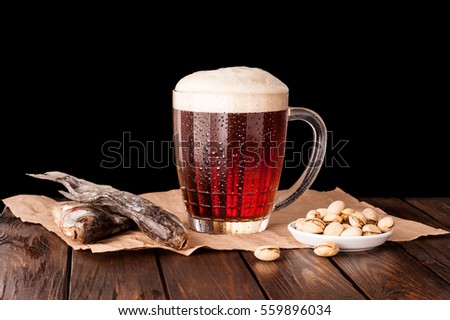 dark cold beer in a frosty mug on dark wooden table. dry fish, pistachios on paper