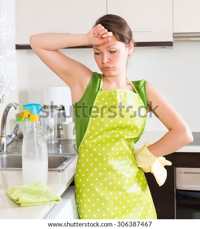 Sad girl cleaning furniture in kitchen at home