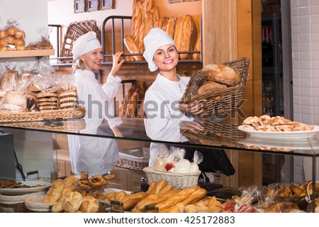 Friendly smiling female bakers selling fresh pastry and loaves in bread section