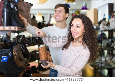 Joyful smiling young couple choosing fashion winter shoes in a shoe store