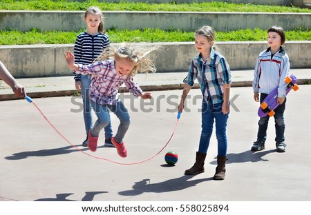 Happy positive children playing skipping rope jumping game and laughing outdoors