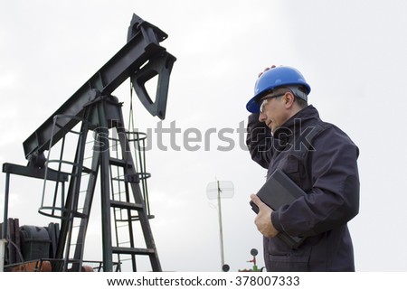 worker on an oil pump keeps the helmet with his hand