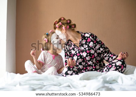 Beautiful young mother and her cute daughter in pajamas and with hair curlers on heads Mother and her daughter child girl playing and hugging.