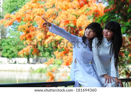 HANOI, VIETNAM, JUNE 12: unidentified Vietnamese girls wear Ao dai near flamboyant tree on June 12, 2011 in Hanoi, Vietnam. Ao dai is famous traditional custume for woman in VIetnam.