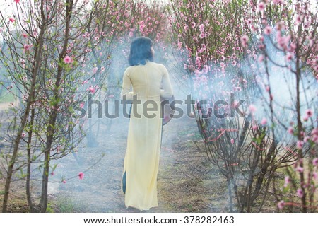 Beautiful Vietnamese girl with traditional dress (ao dai) is in peach flower garden in Hanoi, Vietnam