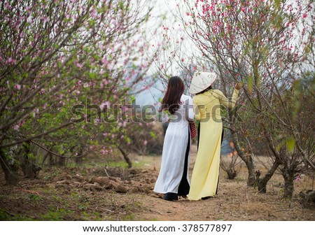 Beautiful Vietnamese girls with traditional dress (ao dai) is in peach flower garden in Hanoi, Vietnam