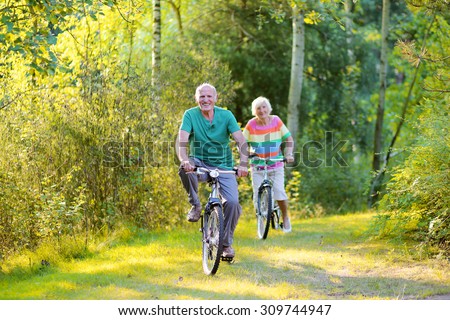 Happy healthy couple biking together in the forest. Seniors enjoying sunny day outdoors. Active retirement concept.