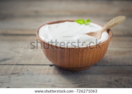 Greek yogurt in a wooden bowl on a rustic wooden table. Selective focus