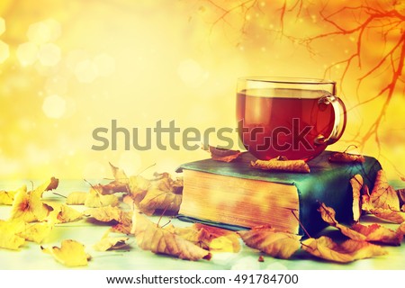 Cup of tea with old book, autumn leaves on wooden table.