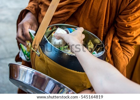 Close up : Give rice food in alms to a Buddhist monk . Hand put food to monk's alms bowl , Thailand. 