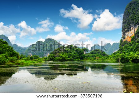 Tropical lake among karst towers at Ninh Binh Province, Vietnam. Blue sky with clouds is visible in background. Ninh Binh Province is a popular tourist destination of Asia.