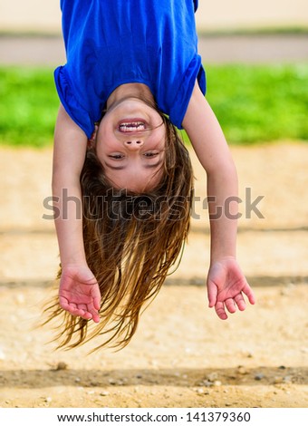 beautiful child hanging upside, laughing, with greenery in the background