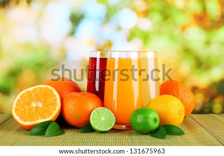 Glasses of juise with leafs and fruits on table on bright background