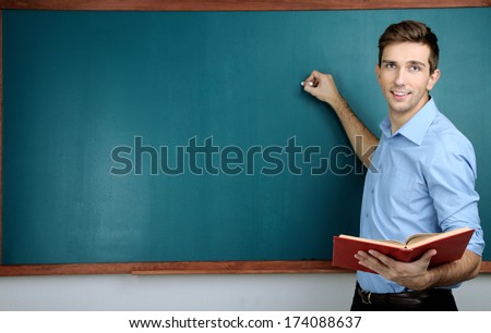 Young teacher near chalkboard in school classroom