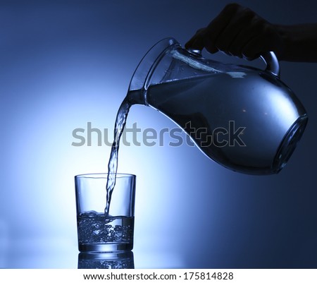 Pour water from pitcher into glass, on dark blue background - stock photo