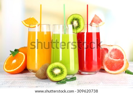 Glasses of different juice with fruits and mint on bright background