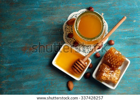 Honeycomb, glass pot with honey and nuts on color wooden background