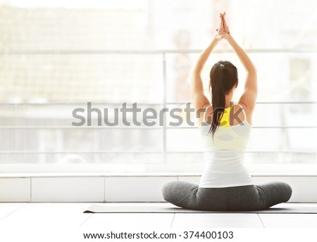 Health concept. Young attractive woman does yoga exercise in the gym against window