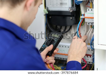 Young electrician measuring voltage in fuse board