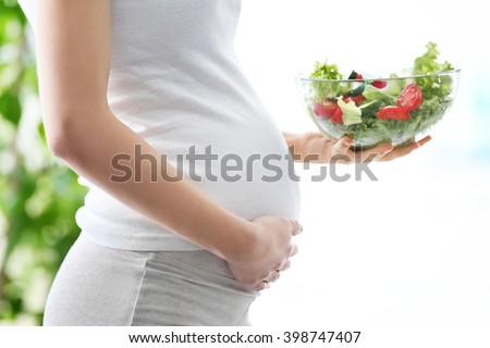 Pregnant woman holding glass bowl with fresh salad
