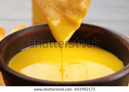 Dipping chips into bowl with creamy cheese sauce, close up