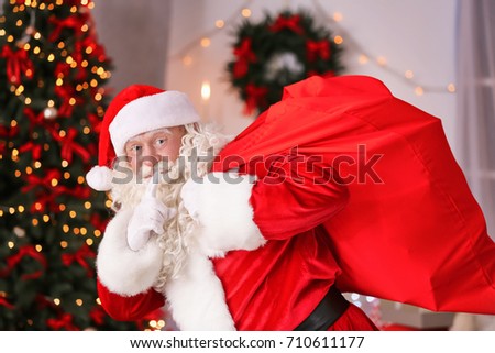 Authentic Santa Claus with big red bag full of gifts against blurred Christmas lights