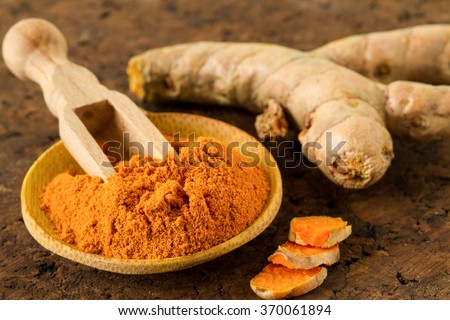 Turmeric root and turmeric powder on wooden background