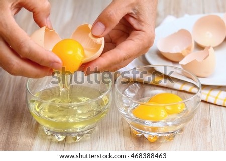 Woman hands breaking an egg to separate egg white and yolks and egg shells at the background 
