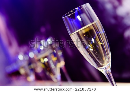 Glass with champagne lit by nightclub lights on dark-purple background