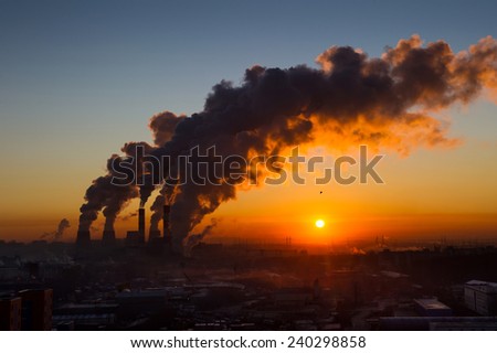 Power plant pipes with swirling smoke at sunrise. Environmental pollution. View against the sun.