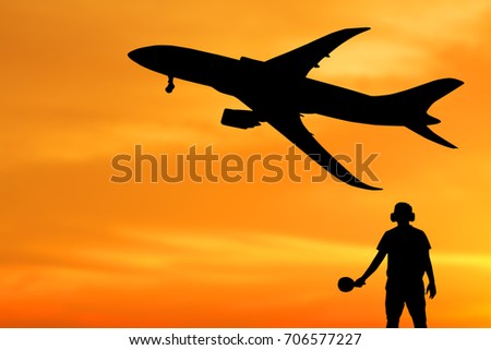 Silhouette of ground staff sending airplane taking off flight with orange sky background