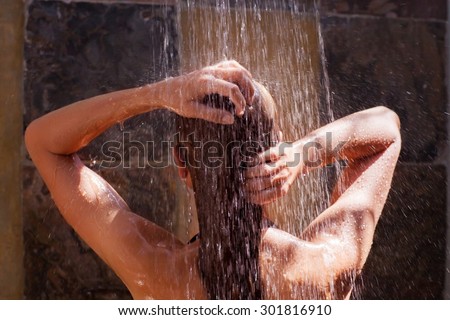Woman in the shower, back side of young female showering under refreshing water, healthy lifestyle, enjoying time in luxury spa resort