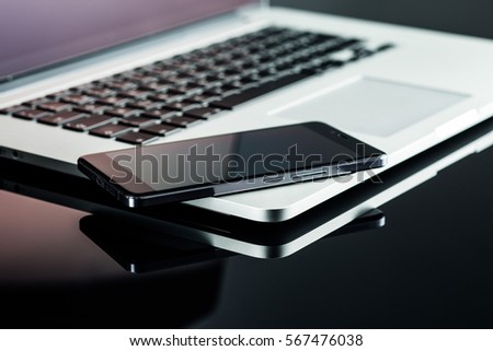 Smartphone and laptop on black table.