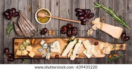 Cheese selection on wooden rustic board. Cheese platter with different cheeses, grapes, nuts, honey and dates on weathered wood background.