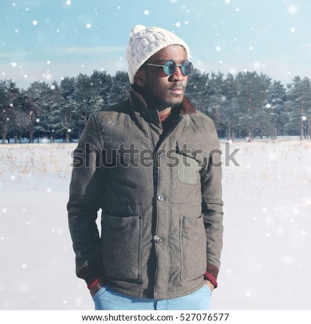 Fashion winter young african man wearing sunglasses and jacket with knitted hat over snowflakes