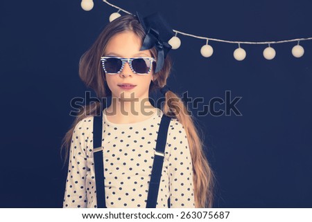 Fashion photo of young hipster child wearing cool clothes and sunglasses standing over dark wall, instagram toned image