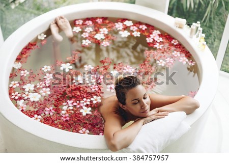 Woman relaxing in round outdoor bath with tropical flowers, organic skin care, luxury spa hotel, lifestyle photo, top view