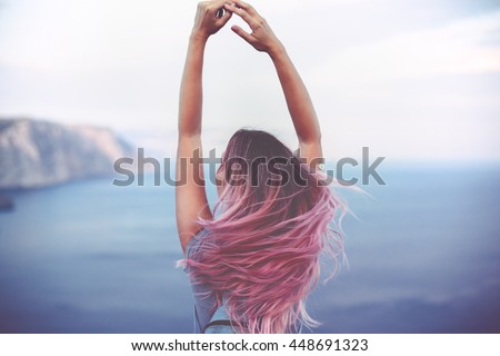 Woman with pink hair standing on the mountain top over blue sea view, photo toned