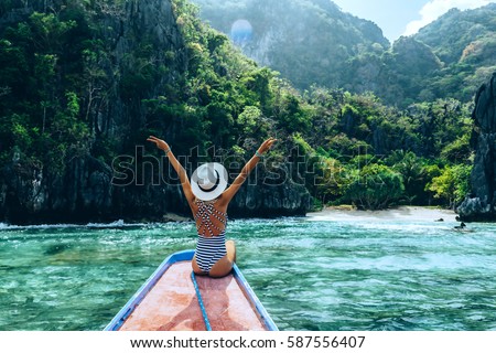 Back view of the young woman in hat relaxing on the boat and looking at the island. Travelling tour in Asia: El Nido, Palawan, Philippines.