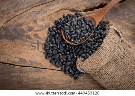 Sack of black beans spill beans with black beans in a wooden spoon on wooden table.