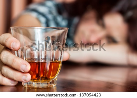 Drunk woman holding an alcoholic drink and sleeping with her head on the table (Focused on the drink, her face is out of focus)
