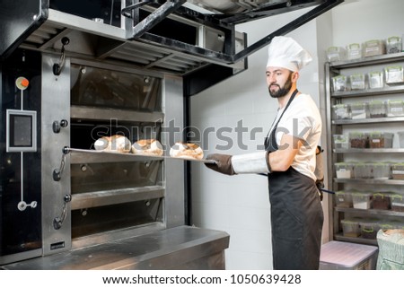 Baker taking off baked breads with shovel from the professional oven at the manufacturing