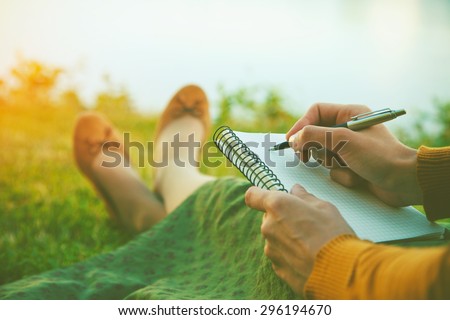 female hands with pen writing on notebook on grass outside