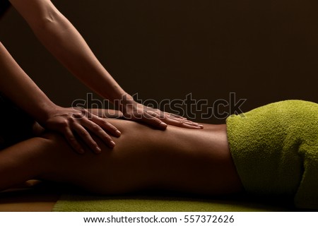 close-up masseur hands doing back massage in spa center. low key photo