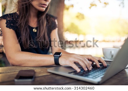 Young woman wearing smartwatch using laptop computer. Female working on laptop in an outdoor cafe.